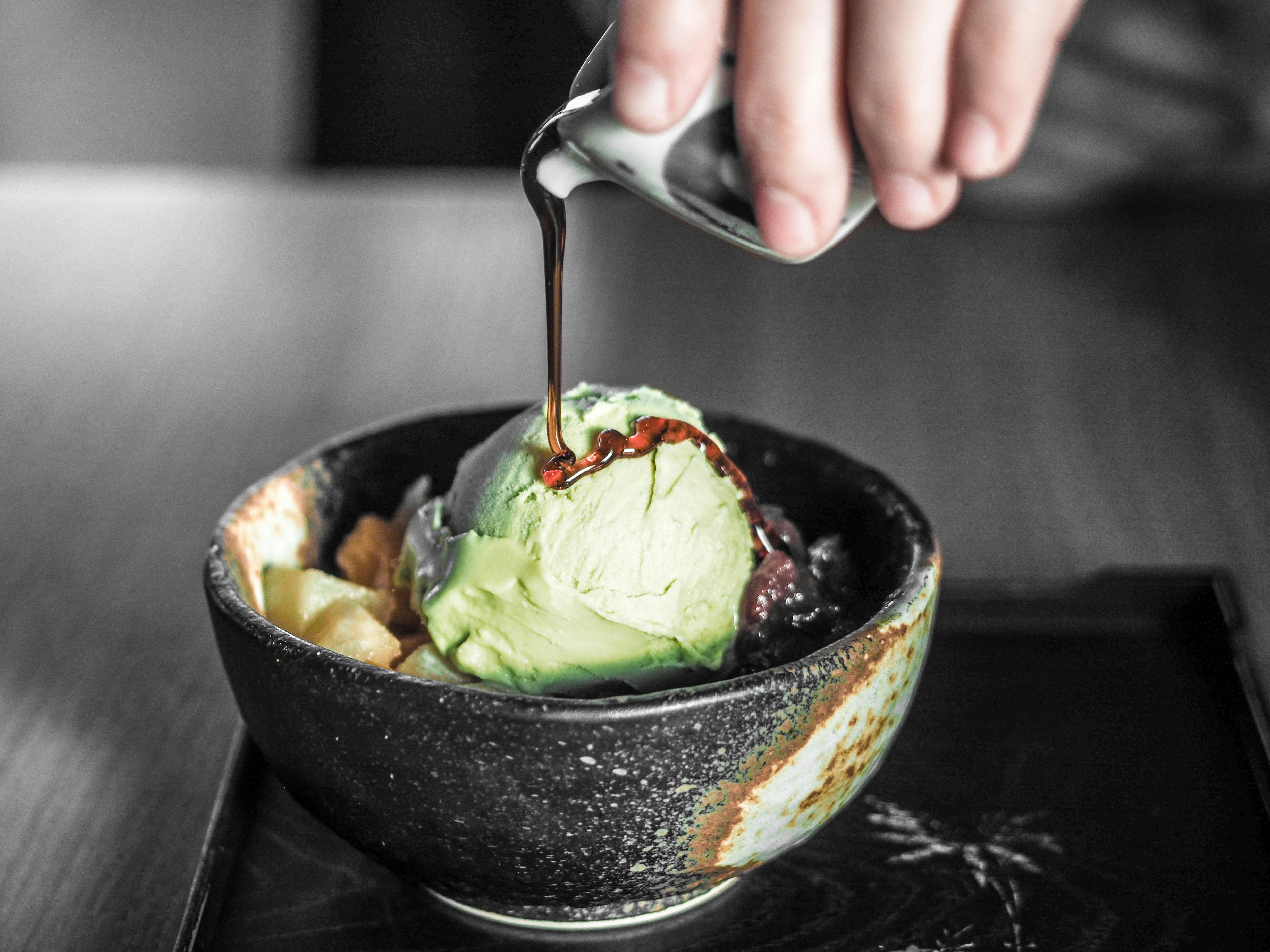 An image of green matcha ice cream in a black bowl with syrup being poured over it.